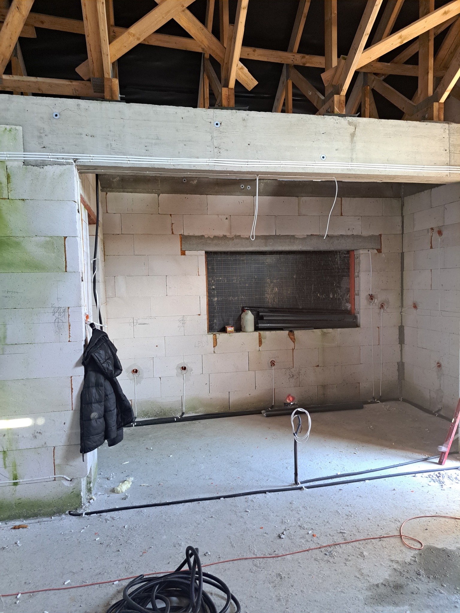 Wnętrze w trakcie remontu z widoczną instalacją elektryczną: kable prowadzone po ścianach z pustaków i pod sufitem, puszki instalacyjne w ścianach, drewniana konstrukcja dachu.