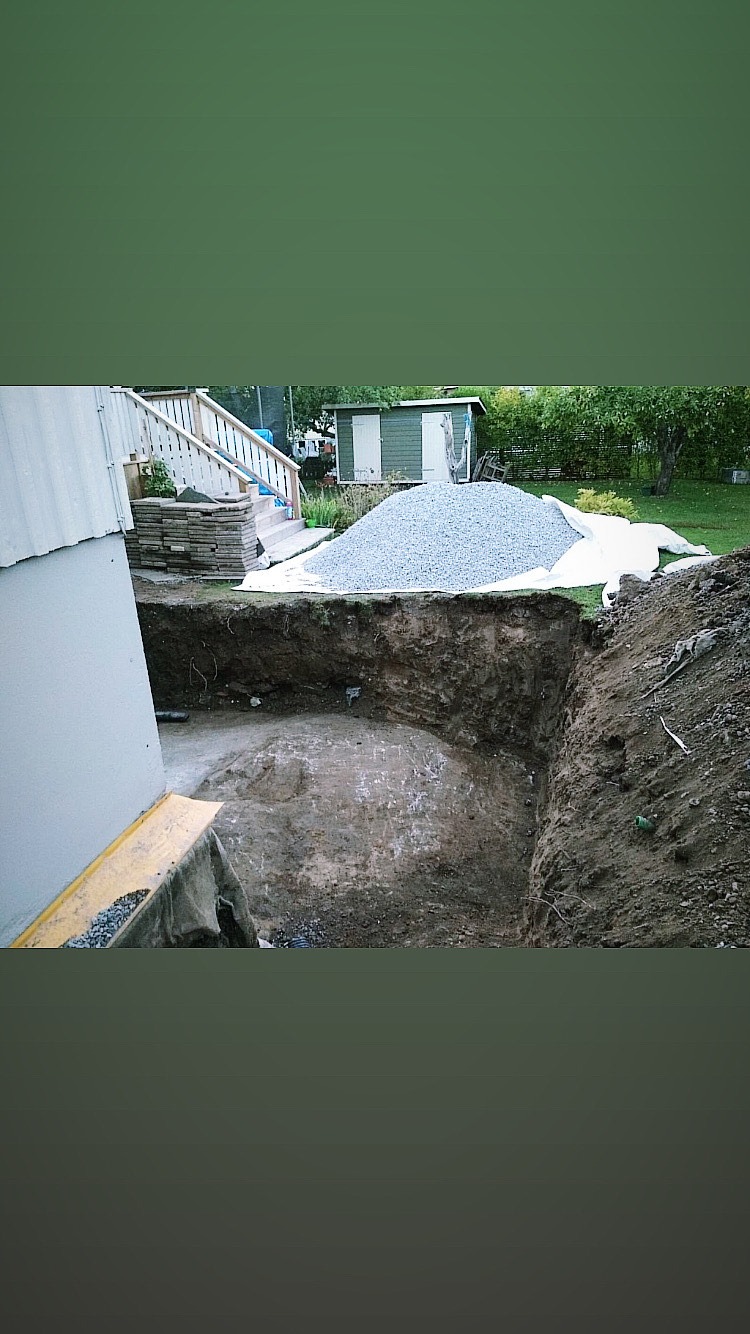 Wykop ziemny w ogrodzie, przygotowany pod budowę, z widoczną stertą gruzu i częścią domu w tle.