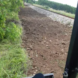 Przygotowanie terenu pod torowisko kolejowe, świeżo wyrównana ziemia, widok z kabiny maszyny budowlanej, na pierwszym planie fragment lemiesza.