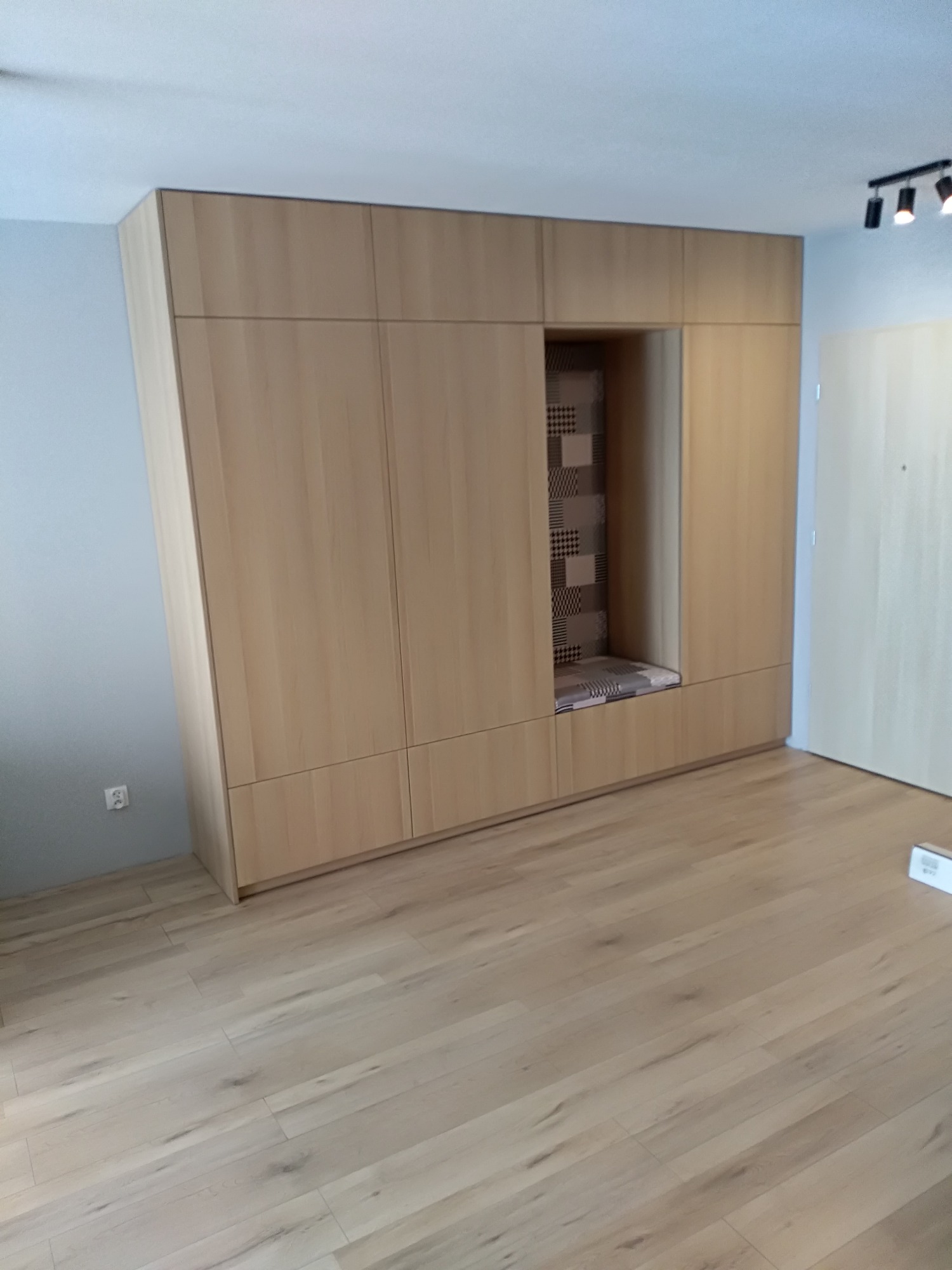 Jasna zabudowa meblowa z wnęką do siedzenia z wzorzystym obiciem, dopasowana do koloru podłogi z paneli.