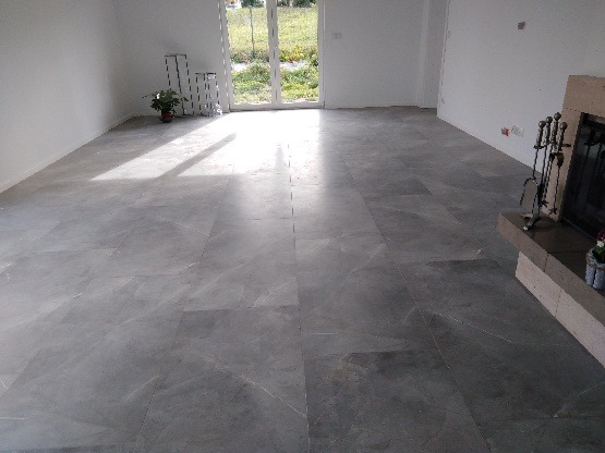 Wykończona posadzka z szarej, polerowanej płyty w jasnym, pustym pomieszczeniu z kominkiem i dużym oknem balkonowym.