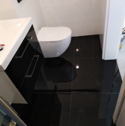 Nowoczesna łazienka z czarną, błyszczącą podłogą, białą toaletą podwieszaną i szafką pod umywalkę z chromowanymi uchwytami, widok z góry.