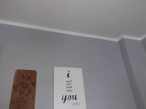 Pomieszczenie z szarą ścianą, białą listwą przysufitową, plakatem z napisem i drewnianą dekoracją. Ściana pomalowana na jednolity, matowy kolor.