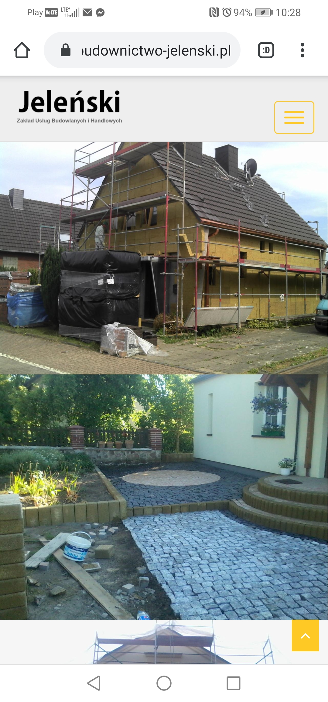 Dom w trakcie ocieplania, widoczne rusztowania i materiały izolacyjne, na dole fragment układanej kostki brukowej z widocznym wiadrem po kleju.