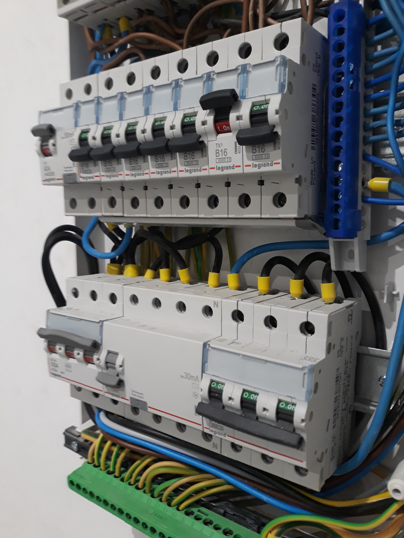 Rozdzielnica elektryczna z zainstalowanymi bezpiecznikami i przewodami. Widoczne przewody w różnych kolorach oraz listwy zaciskowe. Bezpieczniki marki Legrand.