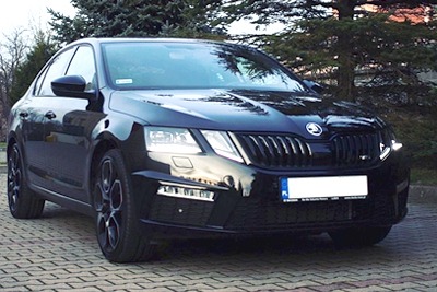 Czarna Skoda Octavia z czarnymi felgami, zaparkowana na brukowanej powierzchni, z widocznym przodem i bokiem auta.
