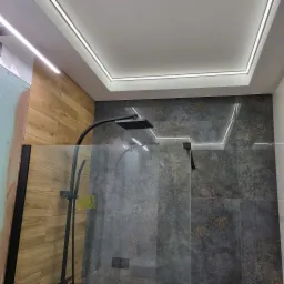 Nowoczesna kabina prysznicowa z deszczownicą, szklaną ścianką i podświetlanym sufitem z drewnopodobnymi i szarymi płytkami.