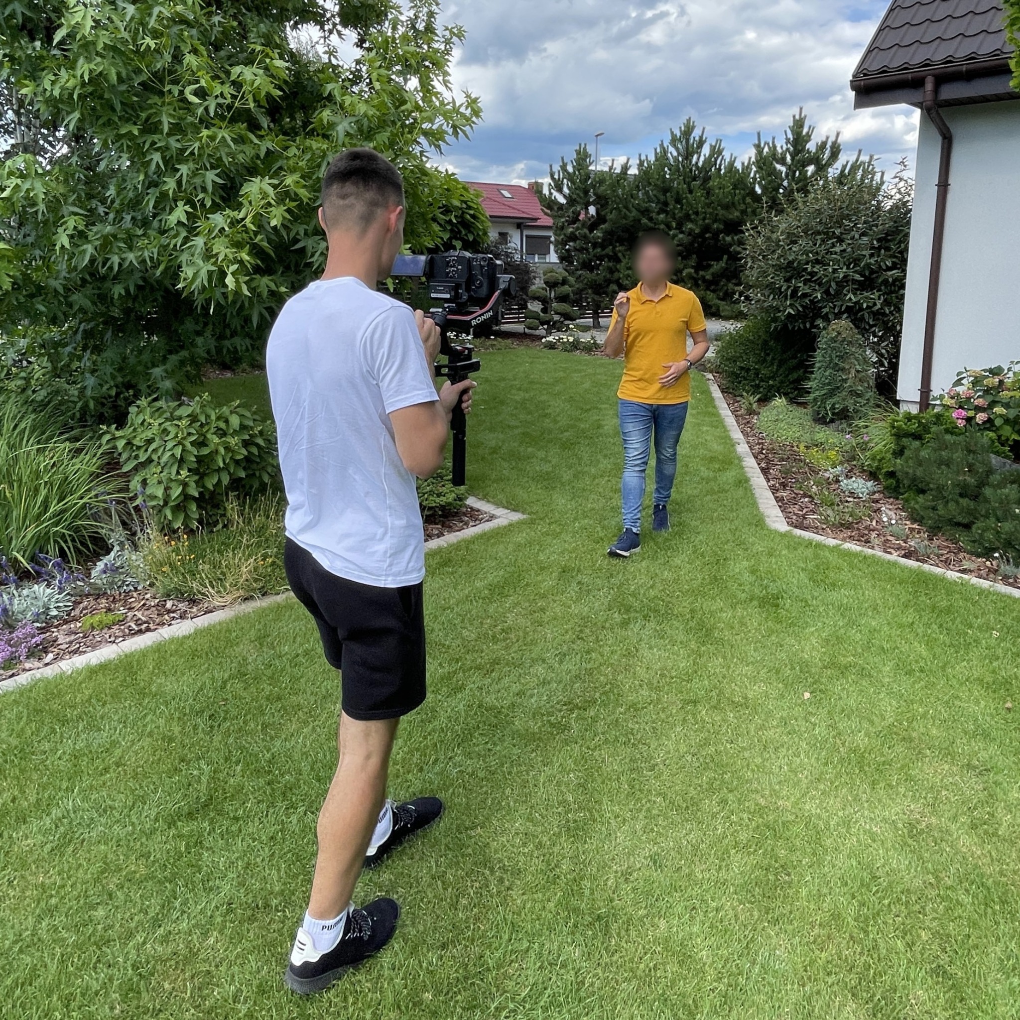 Operator kamery stabilizacyjnej Ronin filmuje mężczyznę w żółtej koszulce na tle zadbanego ogrodu przydomowego.
