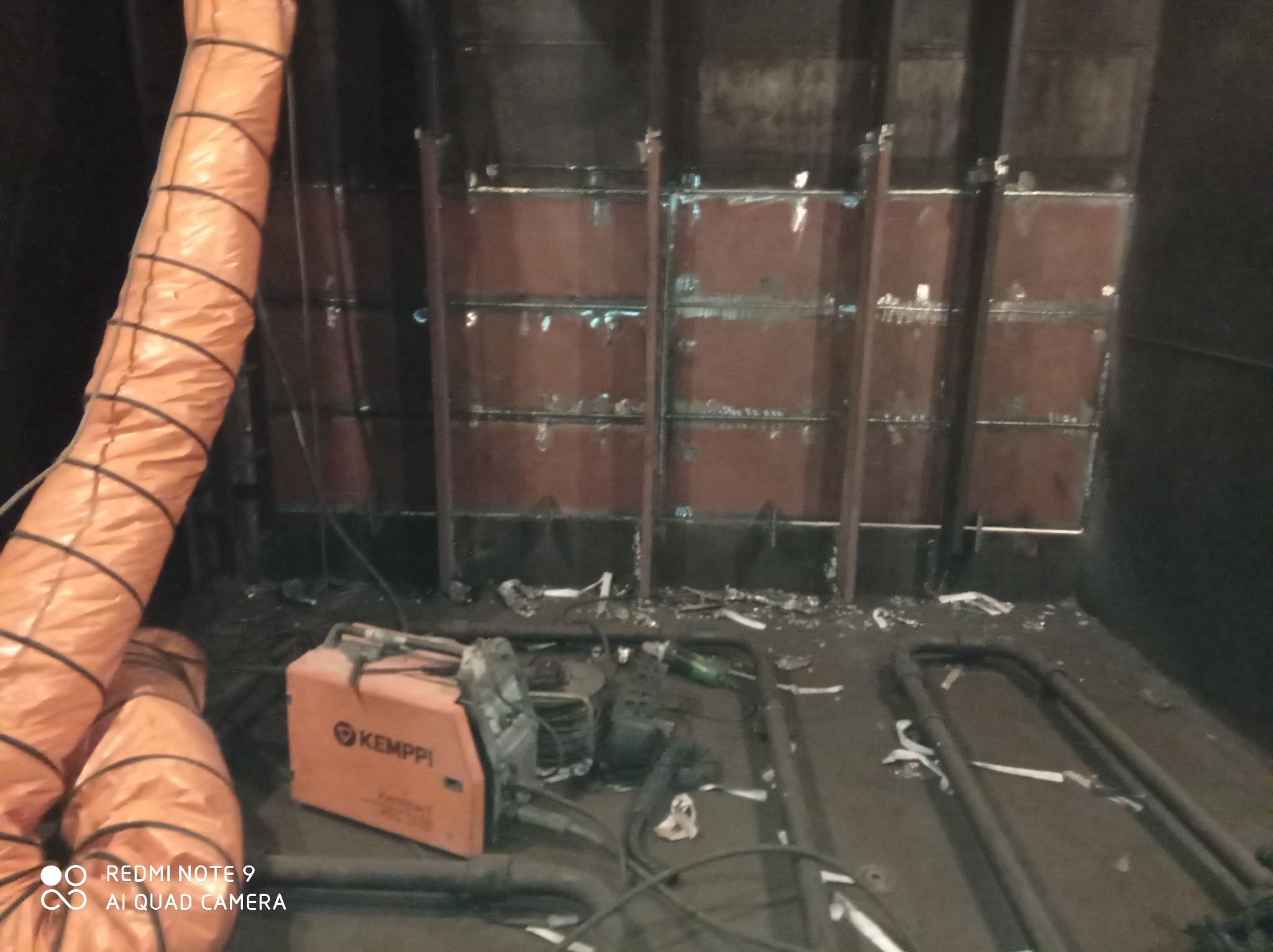 Wnętrze w trakcie prac spawalniczych z widocznym spawarką Kemppi, przewodami wentylacyjnymi i elementami konstrukcyjnymi ścian.