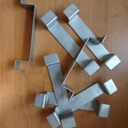 Metalowe, gięte profile ze stali nierdzewnej na drewnianym tle, prawdopodobnie elementy mocujące lub wsporniki.