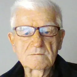 Portret starszego mężczyzny w okularach z siwymi włosami, na neutralnym tle.