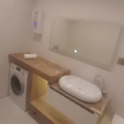 Nowoczesna łazienka z białą umywalką nablatową, pralką pod drewnianym blatem i dużym lustrem bez ramy z podświetleniem LED.