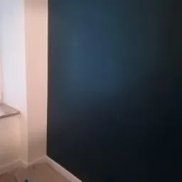 Świeżo pomalowana ściana w odcieniu ciemnego granatu w rogu pomieszczenia, widoczna butelka wody i puszka farby na podłodze.