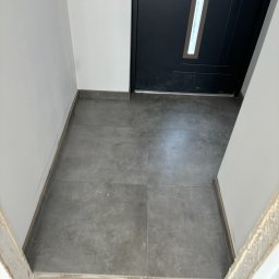 I-TECH - Szare płytki podłogowe w przedpokoju, widok z góry. Minimalistyczny design, ciemna stolarka drzwiowa, białe ściany. Nowoczesne wykończenie wnętrza.