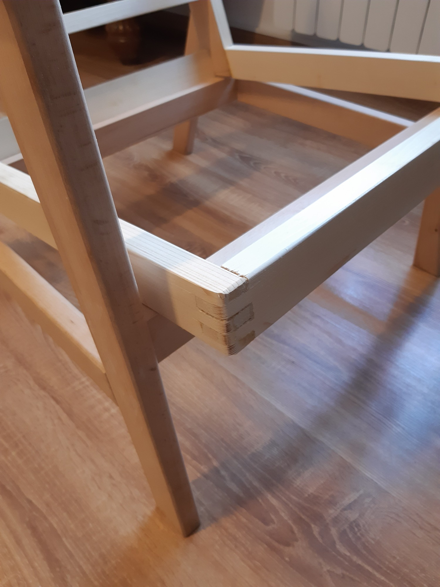 Szczegółowy widok na ramę krzesła z jasnego drewna, z widocznym połączeniem na wpust i czop, wykonaną przez stolarza z Jeleśni, na tle drewnianej podłogi.