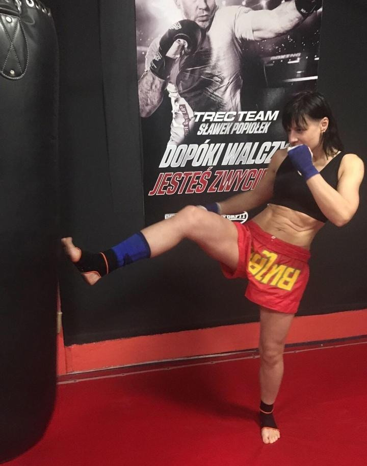 Kobieta w sportowym stroju kopie worek treningowy na tle plakatu z bokserem.