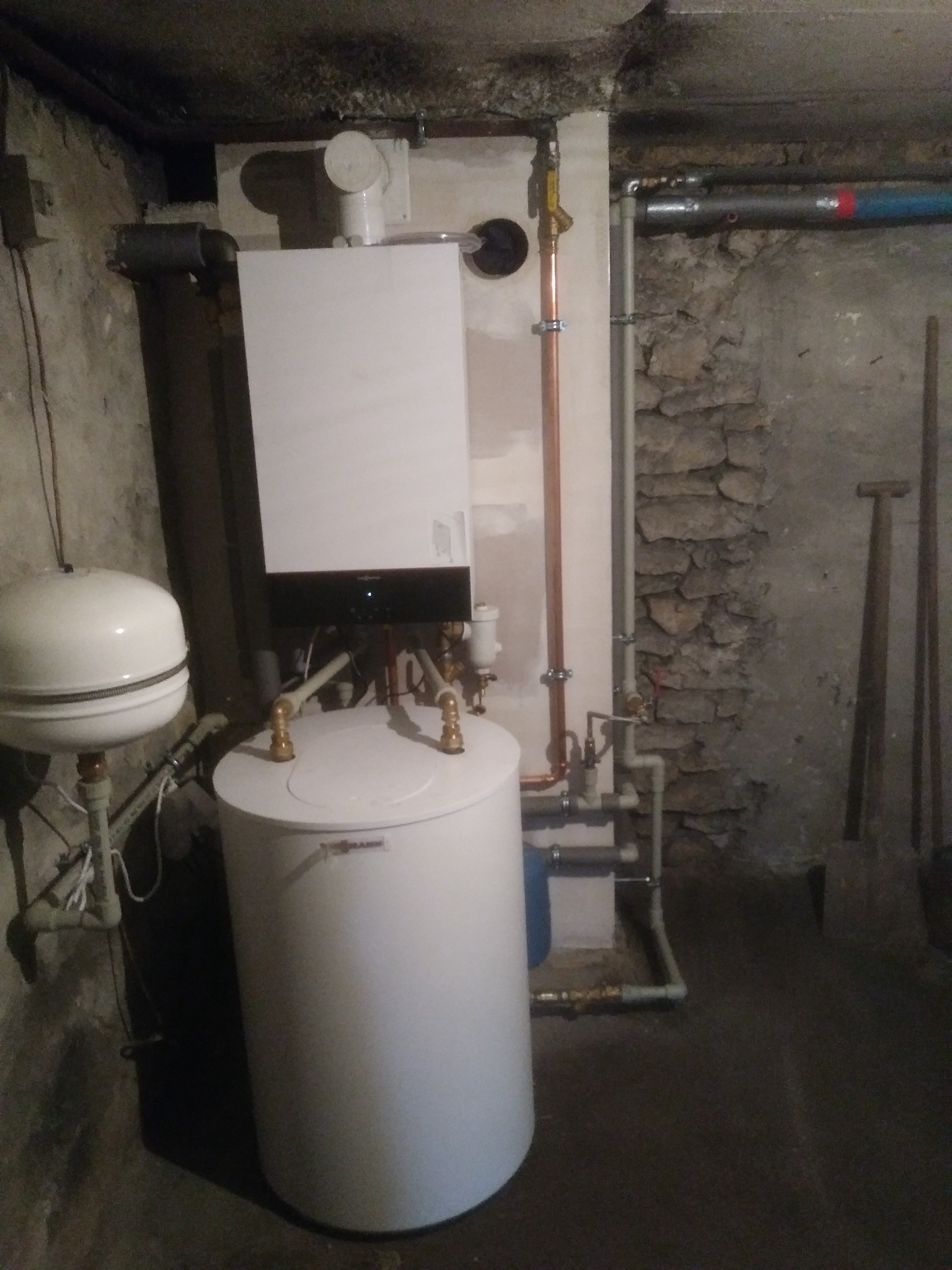 Nowoczesny, biały piec grzewczy Viessmann zamontowany w piwnicy o kamiennych ścianach, z widocznymi rurami miedzianymi i zbiornikiem wyrównawczym.