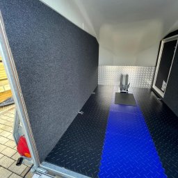 PHU Insidegarage - Wnętrze przyczepy z zamontowanym uchwytem na motocykl, wyłożone wykładziną i antypoślizgową podłogą w kolorze czarnym i niebieskim.