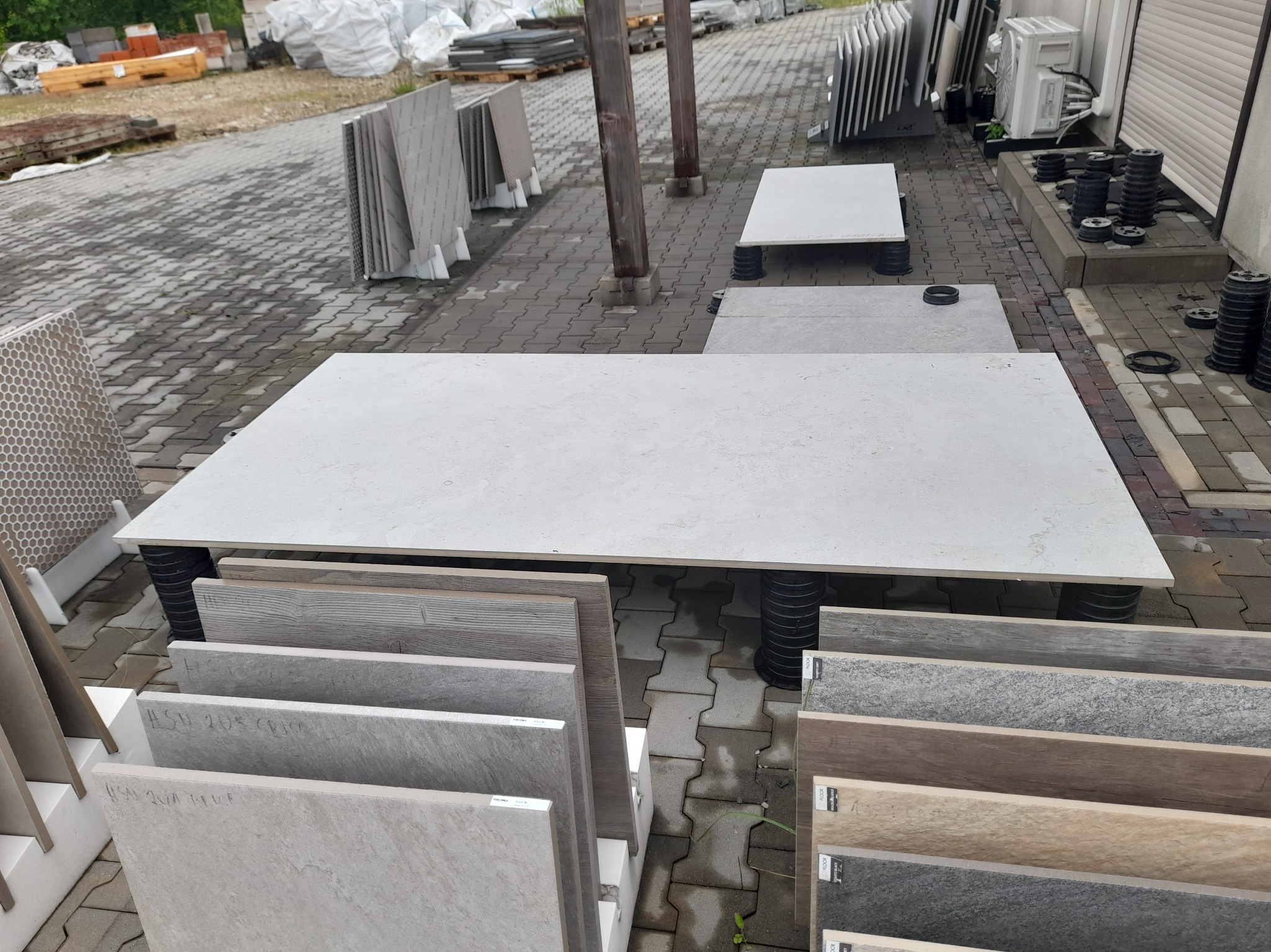 Ekspozycja płyt tarasowych i ceramicznych na zewnątrz. Płyty ułożone na regulowanych wspornikach. Widoczne różne wzory i kolory płytek.