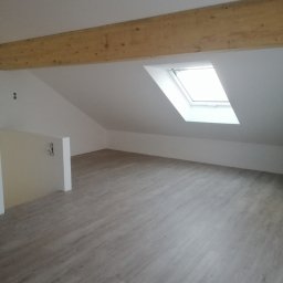 Usługi wykończeniowe - Poddasze po remoncie z jasnymi panelami podłogowymi, drewnianą belką stropową i oknem dachowym w skosie.
