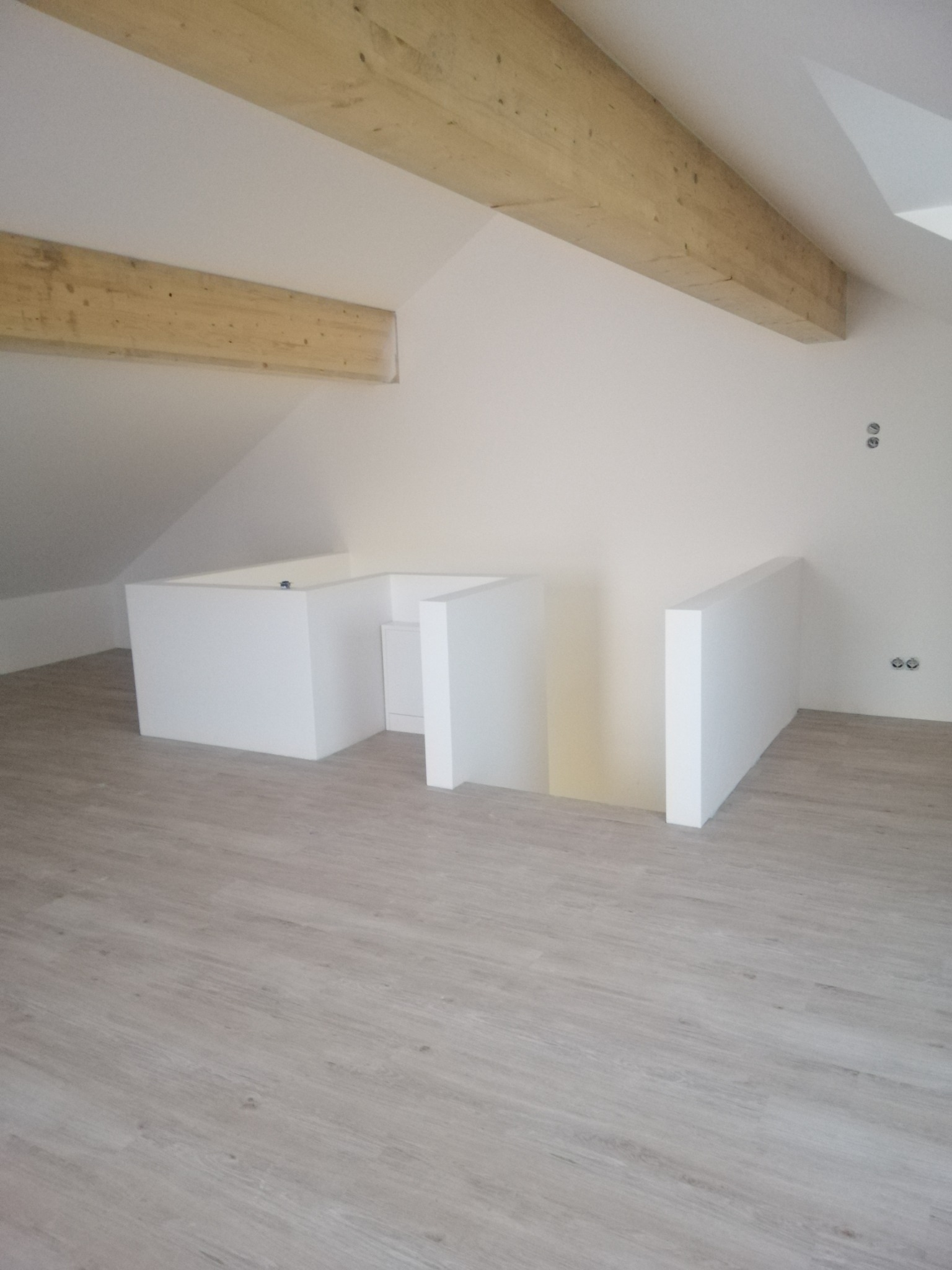 Poddasze po remoncie: jasne panele podłogowe, białe ściany, drewniane belki stropowe, biała zabudowa.