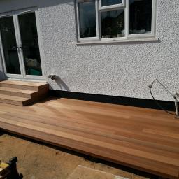 Andrzej Czarkowski - Nowo wybudowany taras z drewna egzotycznego z niskimi schodami przy białej ścianie domu z oknem, widoczna wiertarka akumulatorowa i poziomica.