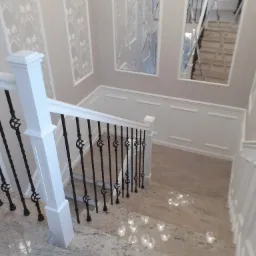 Klatka schodowa z marmurowymi stopniami i kutą balustradą, ściany zdobione sztukaterią i lustrami w ramkach, widok z góry.