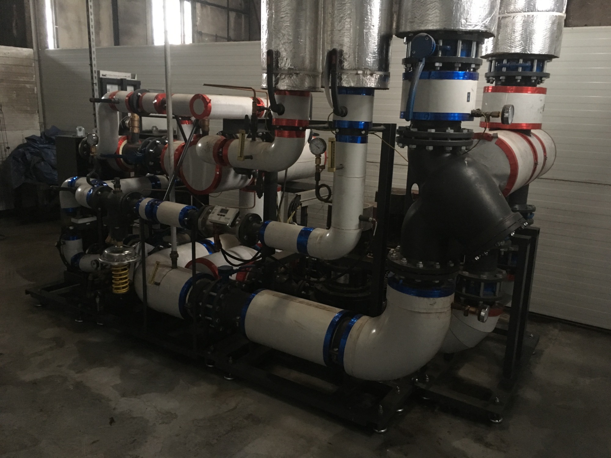 Kompleksowa instalacja przemysłowa z rur, zaworów i izolacji, umieszczona na metalowej ramie w hali produkcyjnej, widoczne liczne przyłącza i manometry.