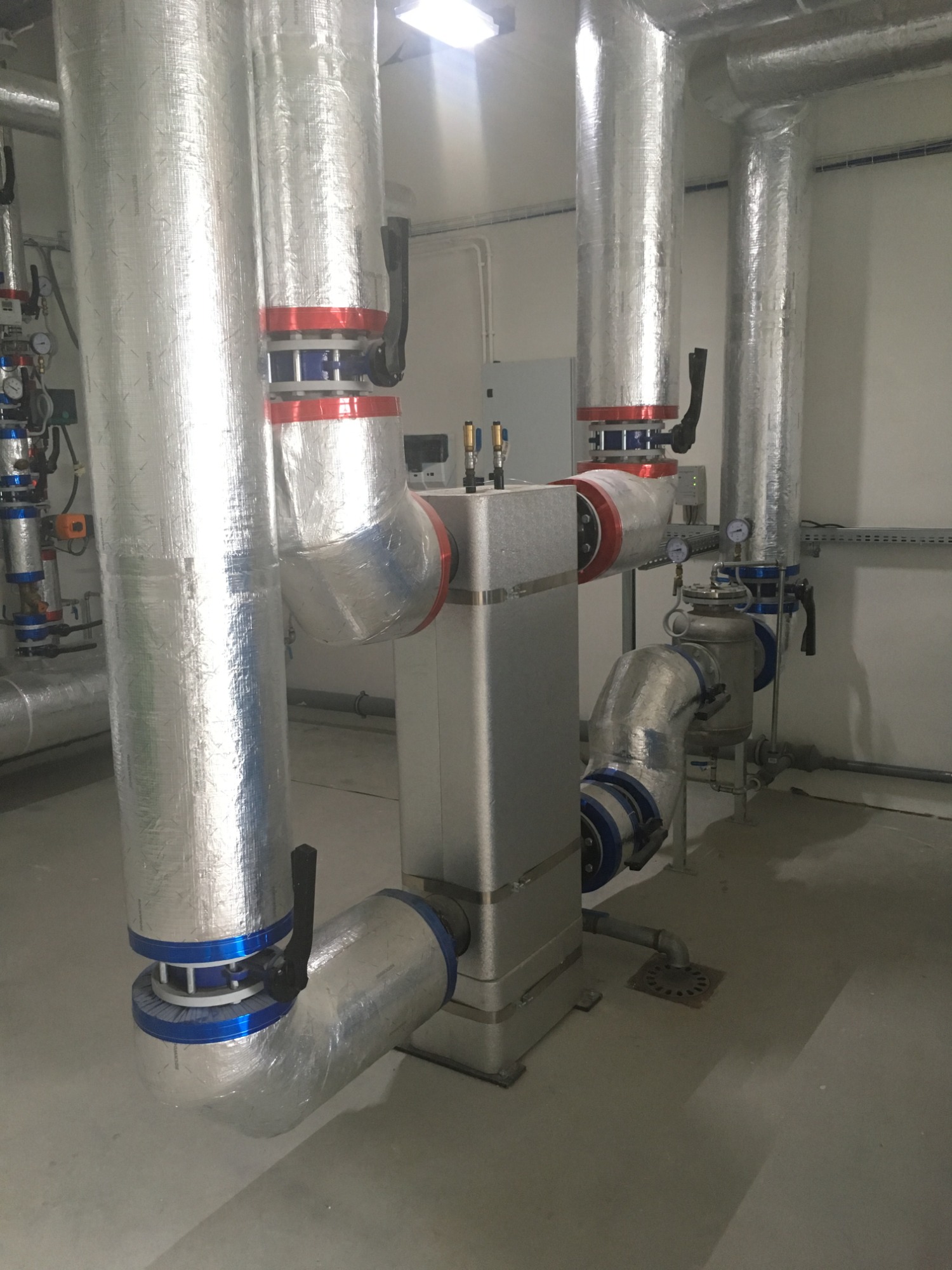 Izolowane rury i armatura w kotłowni przemysłowej, widoczne zawory, manometry i metalowa konstrukcja centralnego urządzenia.