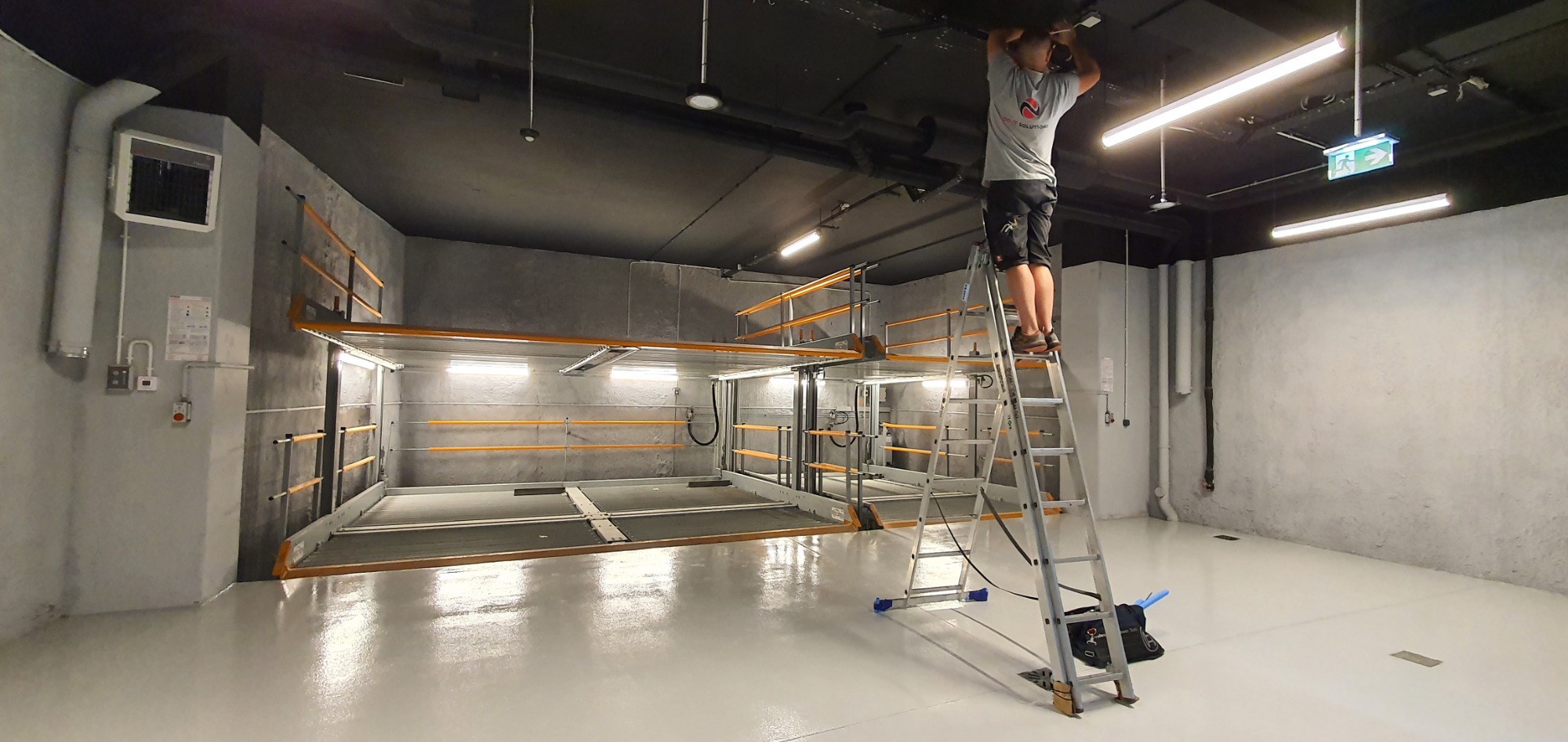 Elektryk na drabinie łączy obwody wentylatorów pod sufitem w nowo wykończonym pomieszczeniu z instalacją wentylacyjną.