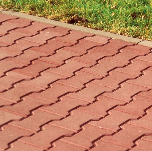 Czerwona nawierzchnia z kostki brukowej typu Behaton ułożona w zygzak, obrzeże z szarego betonu, trawa w tle.