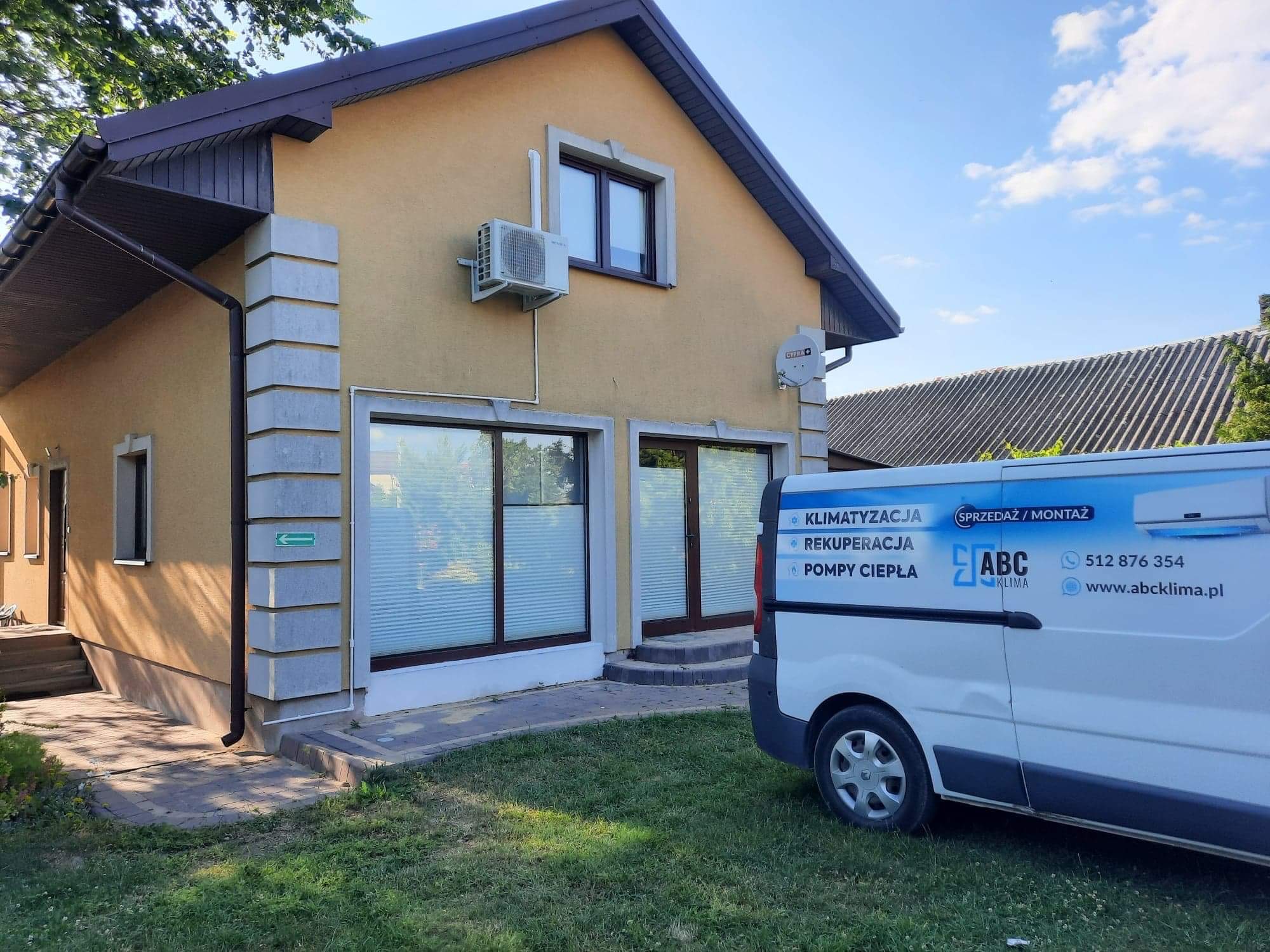 Żółty dom z zamontowaną jednostką klimatyzacji na ścianie, obok zaparkowany biały bus z reklamą firmy oferującej sprzedaż i montaż klimatyzacji, rekuperacji i pomp ciepła.