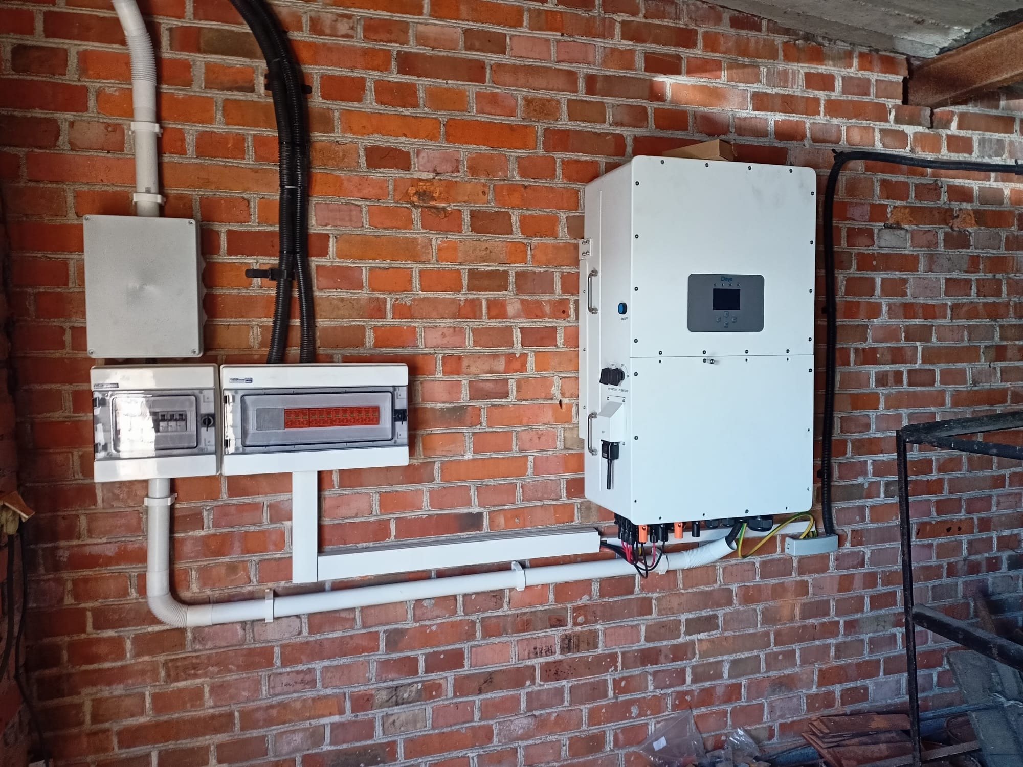 Biała skrzynka z wyświetlaczem i instalacją elektryczną na ceglanej ścianie. Widoczne przewody i rury instalacyjne. Elementy systemu zasilania.