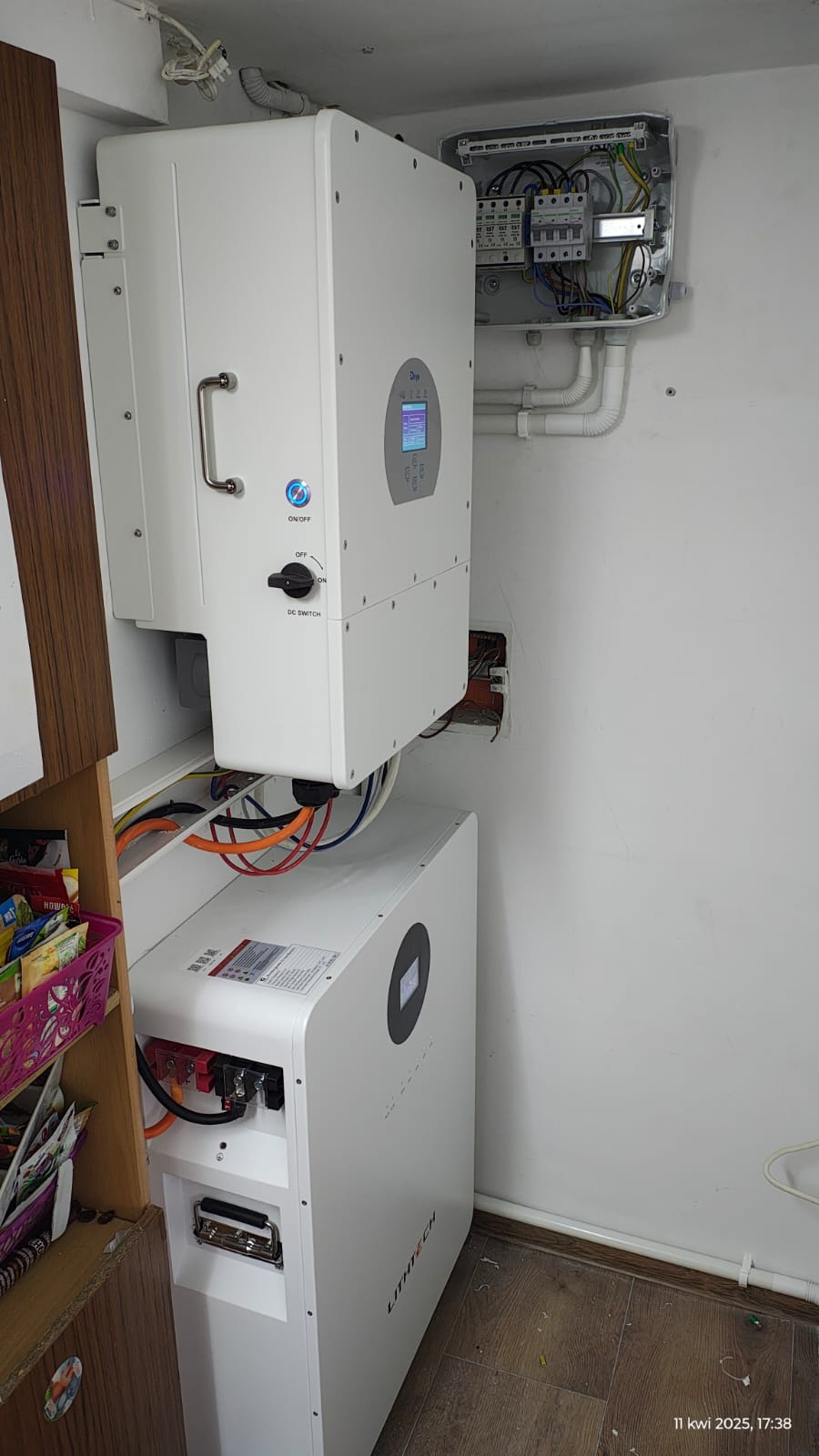 Biały magazyn energii Lithtech i falownik Deye zamontowane na ścianie, widoczna skrzynka z bezpiecznikami i okablowanie, wnętrze pomieszczenia.