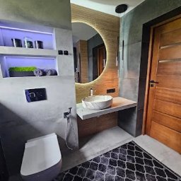 REM-BUD PIOTR SIKORA - Nowoczesna łazienka z okrągłym lustrem z podświetleniem LED, marmurową umywalką i betonową zabudową. Szara armatura i dywan w marokański wzór dopełniają wystrój.