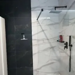 Nowoczesna kabina walk-in z czarną armaturą i płytkami imitującymi marmur. Kontrastujące czarne płytki na jednej ze ścian. Minimalistyczny design.