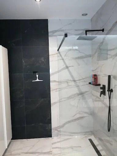 Nowoczesna kabina walk-in z czarną armaturą i płytkami imitującymi marmur. Kontrastujące czarne płytki na jednej ze ścian. Minimalistyczny design.