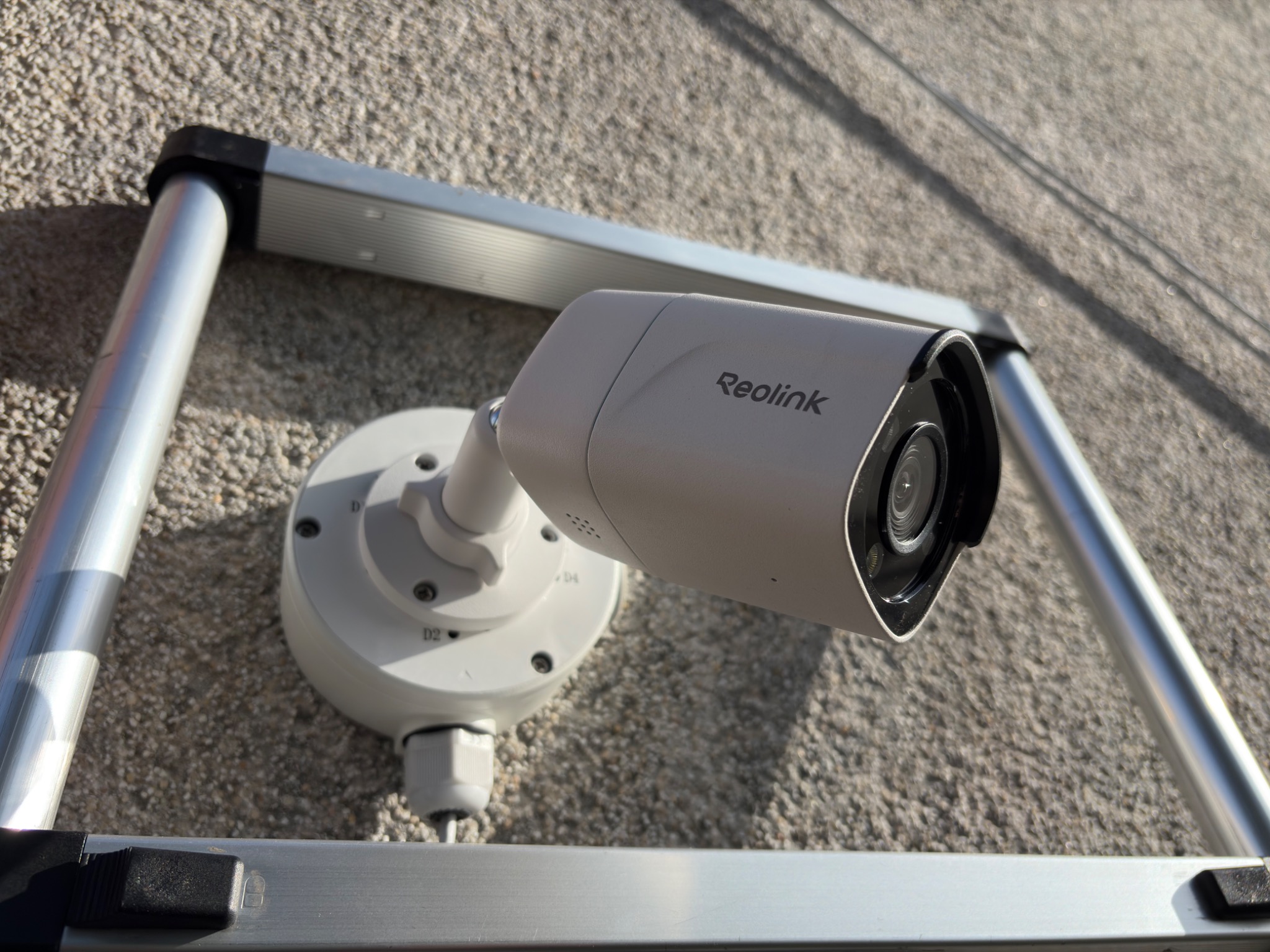 Kamera Reolink zamontowana na elewacji budynku, widoczna z bliska, z elementami drabiny w kadrze. Jasne oświetlenie podkreśla detale urządzenia.