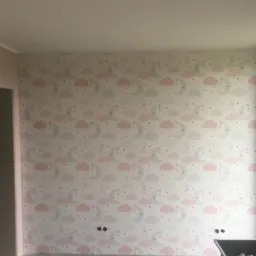 Ściana pokoju dziecięcego po tapetowaniu, pokryta tapetą w pastelowe wzory chmurek i księżyców, widoczne gniazdka elektryczne.