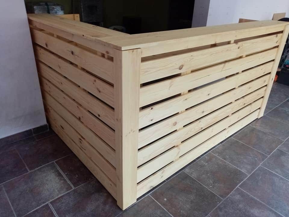 Drewniana lada barowa z jasnego drewna, wykonana z poziomych desek z przerwami, stojąca na ciemnej, ceramicznej podłodze.