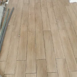 Ułożona podłoga z płytek imitujących drewno, widoczne profile aluminiowe i resztki po montażu przy ścianie.