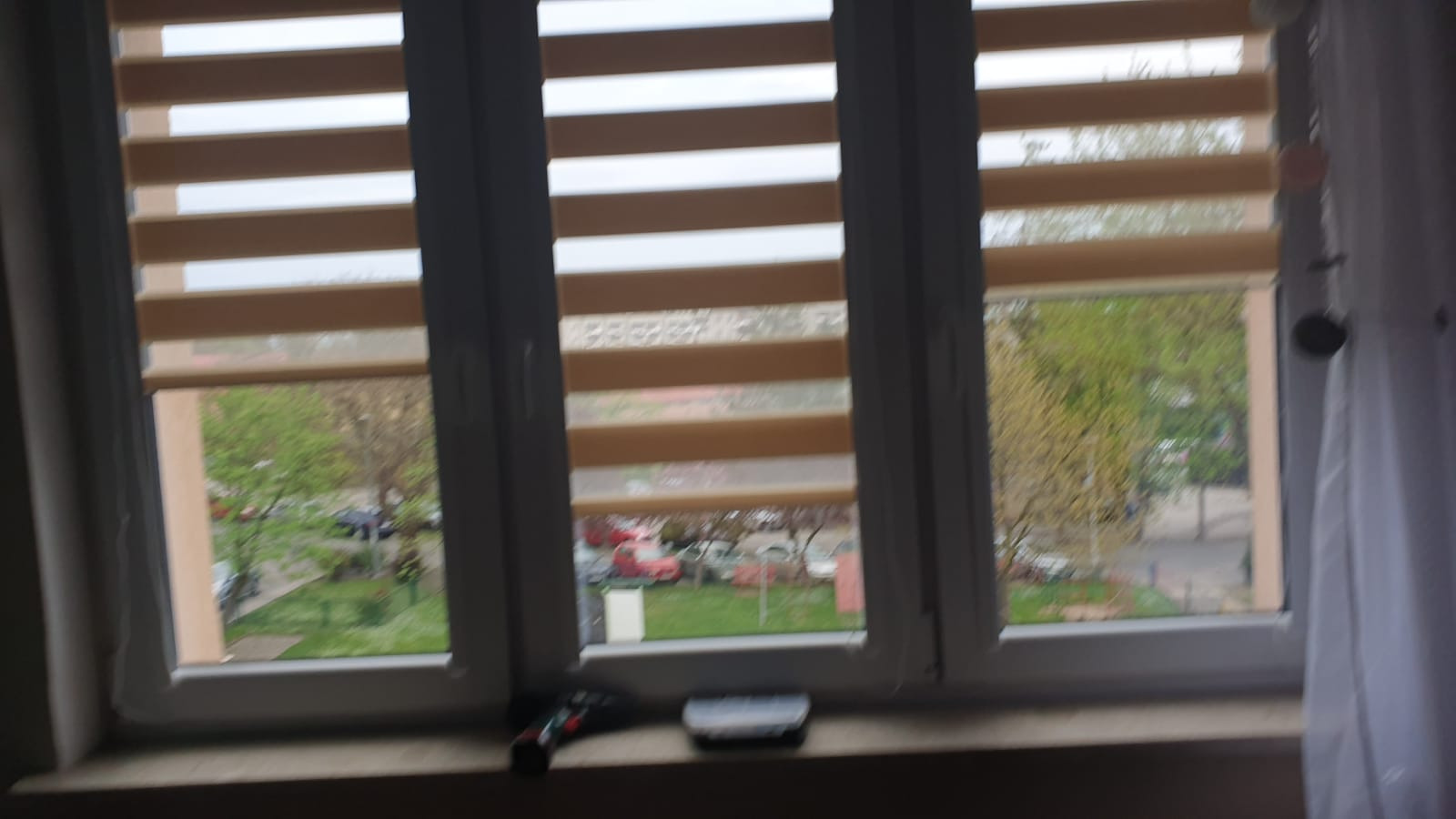 Zamknięte rolety dzień noc w oknie z widokiem na zieleń w Przemyślu, z elementami dekoracyjnymi w rogu okna.