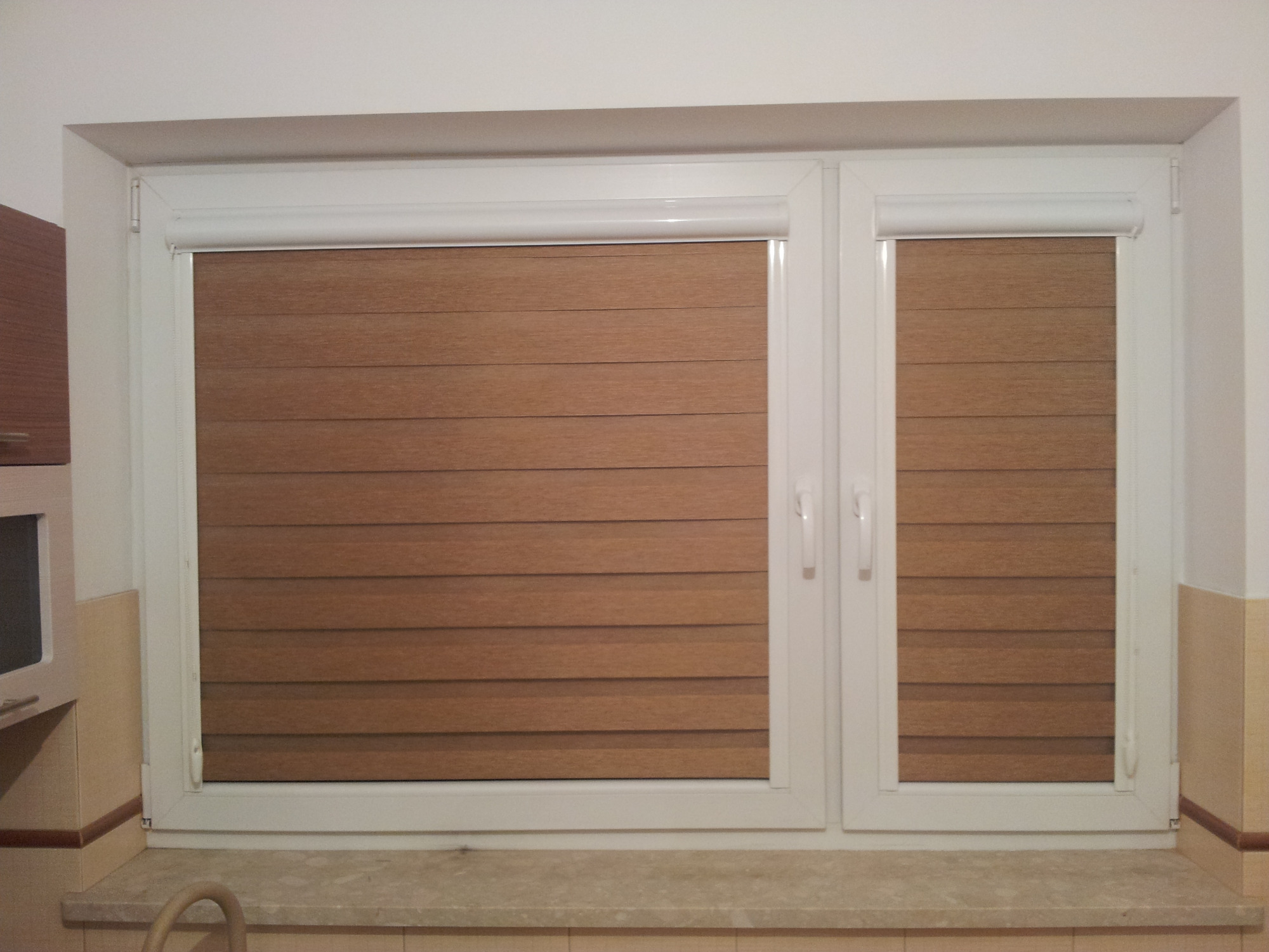 Brązowa roleta dzień noc zamontowana w oknie z białymi ramami, widok z wnętrza pomieszczenia.