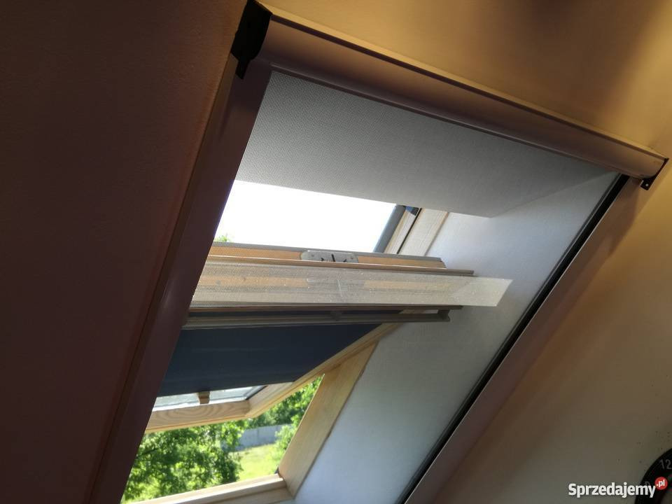 Okna dachowe z zamontowanymi roletami i moskitierą, widok na zewnątrz przez otwarte okno.