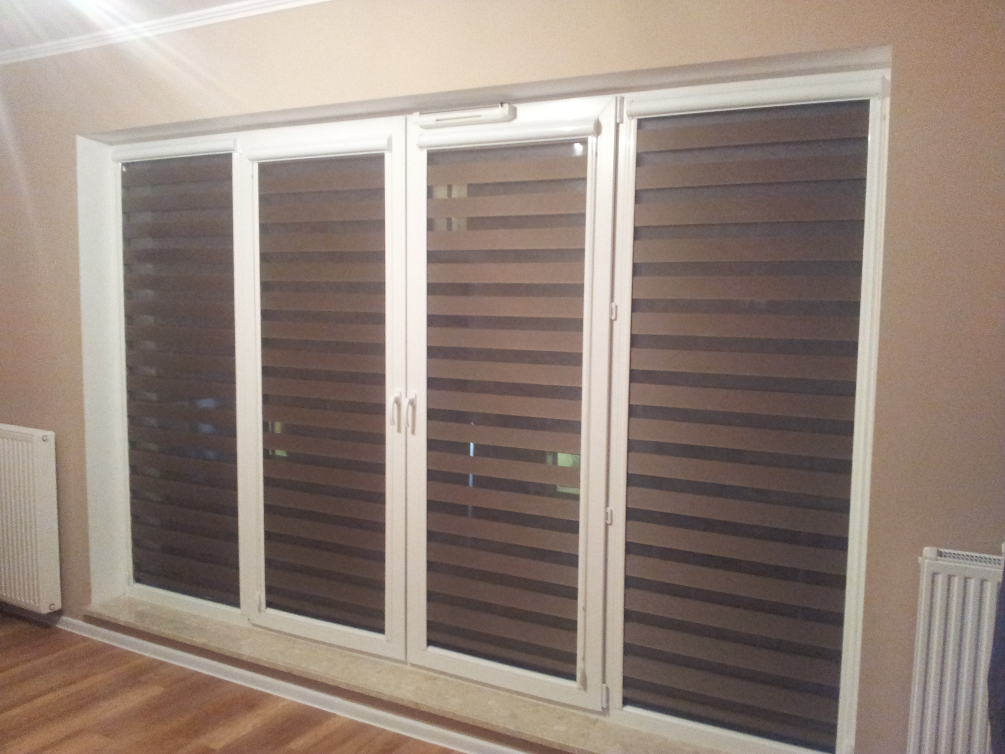 Okno z zamontowanymi roletami dzień-noc w odcieniach brązu i beżu, widoczne poziome pasy regulujące dopływ światła.