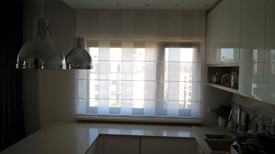 Roleta rzymska w kuchni z widokiem na miasto, oświetlona przez dwie chromowane lampy wiszące.