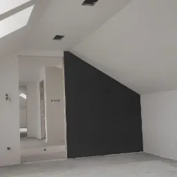 Poddasze po malowaniu: białe ściany i sufit z oknami dachowymi, jedna ściana pomalowana na grafitowo, widoczne puszki elektryczne bez osprzętu, surowa posadzka.