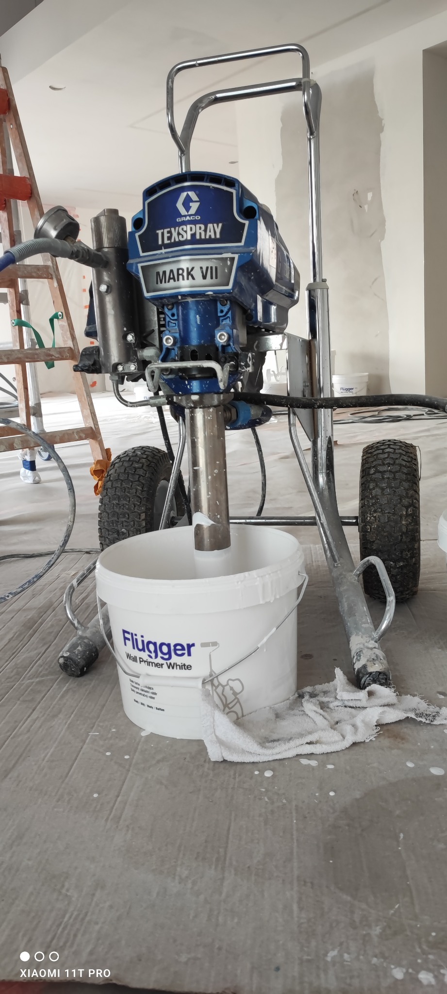 Agregat malarski Texspray Mark VII, wiadro z farbą Flugger Wall Primer White i drabina w tle, przygotowanie do malowania wnętrza.