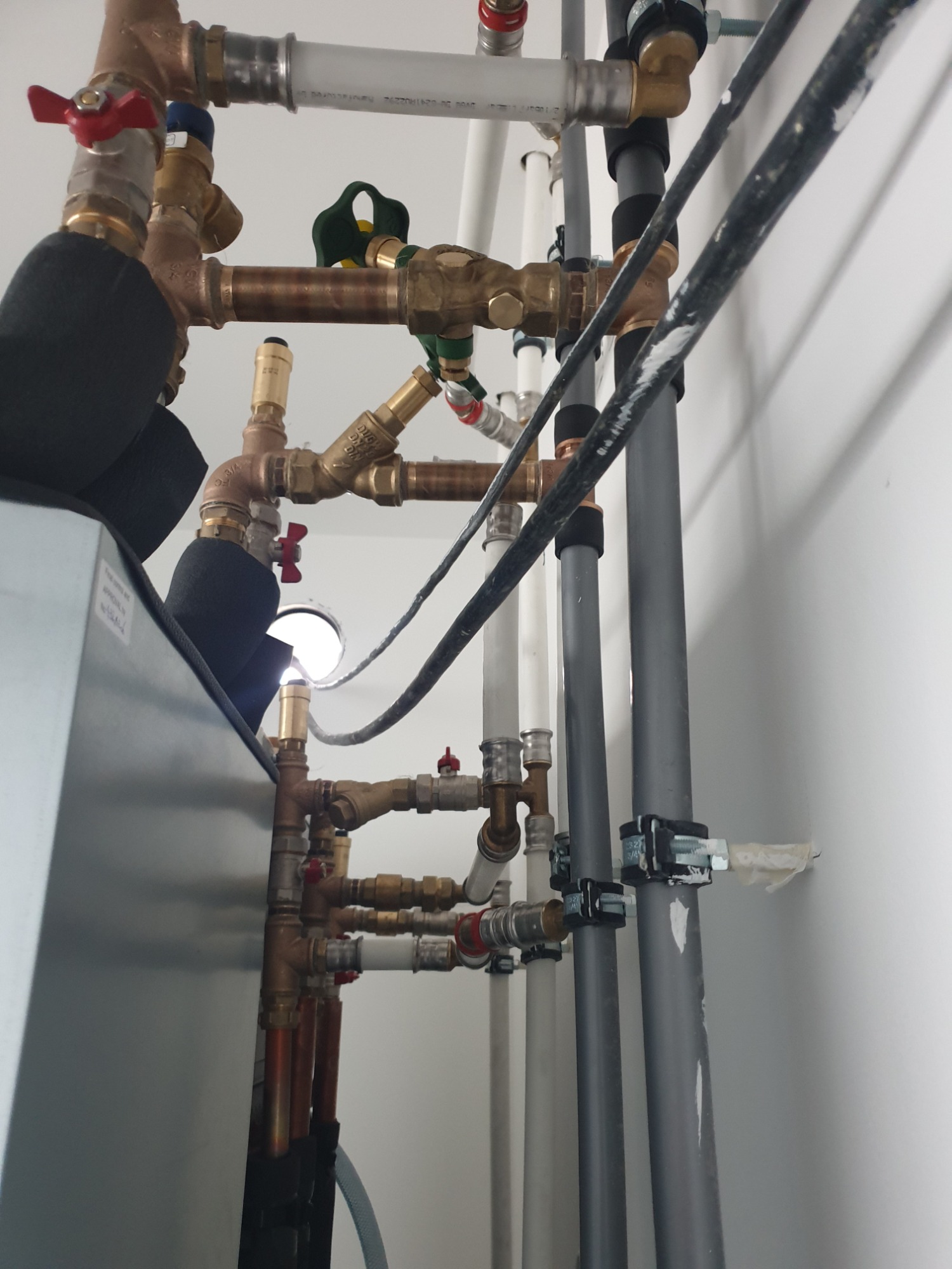 Złożona instalacja hydrauliczna z rur miedzianych i PCV, z zaworami i izolacją termiczną, zamontowana przy białej ścianie w Trzebiatowie.