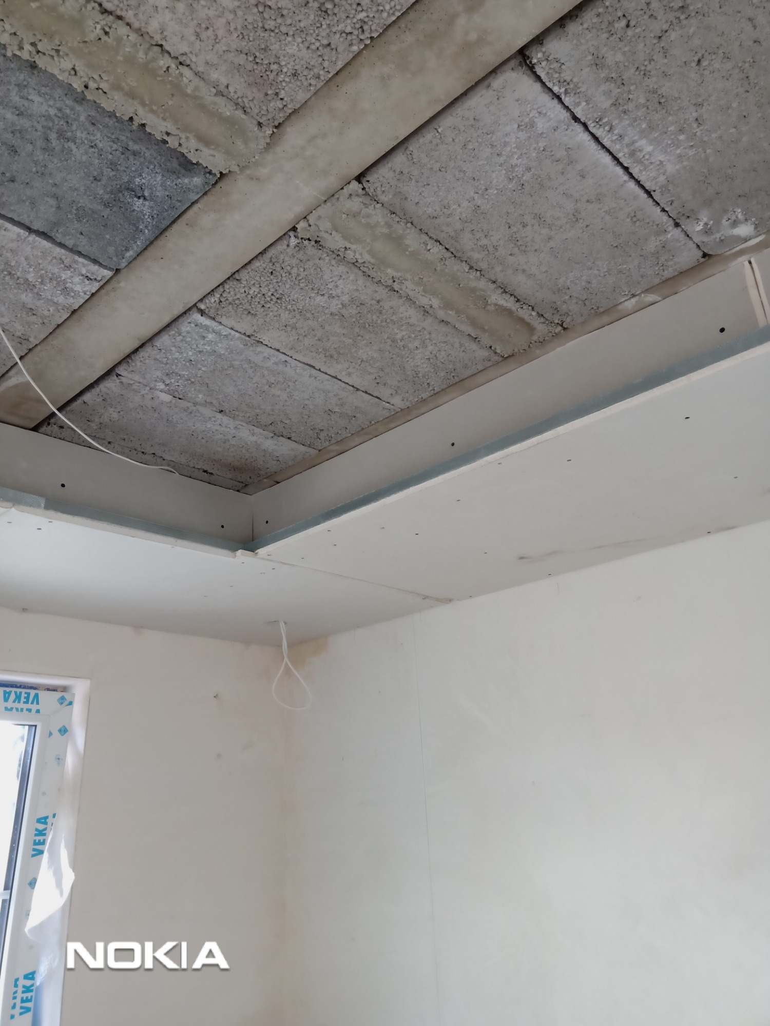 Montaż płyty kartonowo-gipsowej na suficie z widoczną konstrukcją nośną z betonu komórkowego, częściowo zakończony, z widocznymi otworami montażowymi.